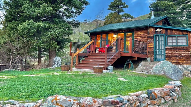 A rustic log cabin with a wooden deck, a staircase, and a stone wall in the foreground. - Storybook Cabin - Private Stream, Incredible Canyon View, Starlink Internet (Bellvue)