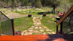 A wooden deck with a stone pathway leading to a grassy area with potted plants and a view of a mountainous landscape. - Storybook Cabin - Private Stream, Incredible Canyon View, Starlink Internet (Bellvue)