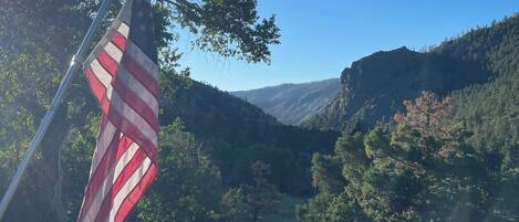 Un asta con la bandera estadounidense en un paisaje natural con montañas y árboles.