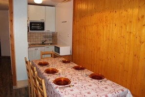 A dining area with a table set for four, wooden paneling on the walls, and a kitchen in the background. - 100m from resort center, 3rd floor, balcony, tv, 48m², Val Thorens (Val Thorens)