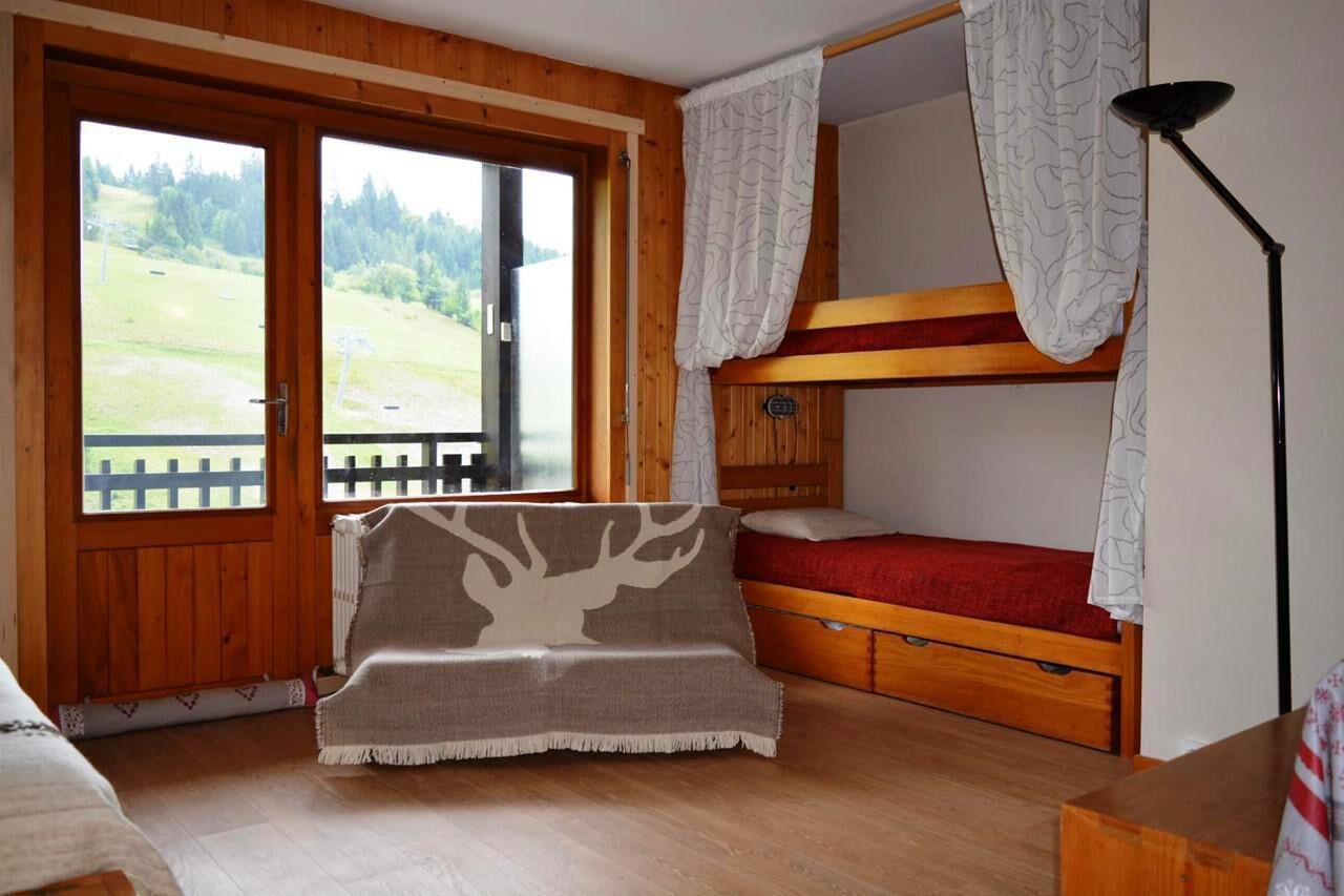 Habitació acollidora amb un llit superposat, un sofà amb llençol estampat de faó i vista a un paisatge verd a través d'una finestra gran.