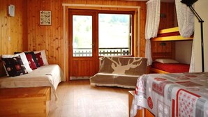 Quarto de cabana de madeira com uma cama, um sofá e uma cama beliche. Há uma janela com vista para árvores e um cercado.