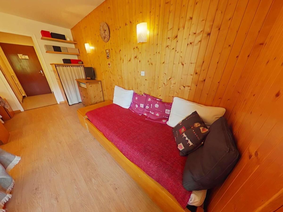 Una habitación con paneles de madera, una cama, una mesita y una estantería con adornos.