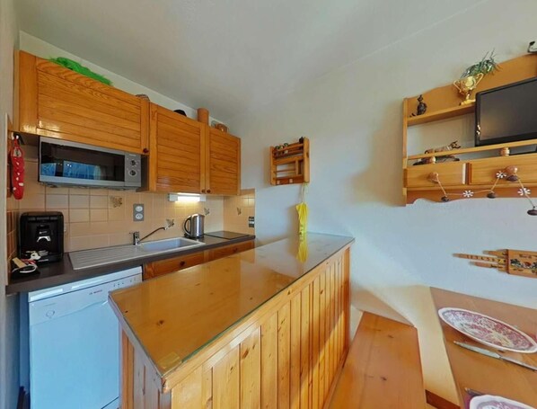A kitchen with wooden cabinets, a microwave, a sink, and a small island with a glass top. - Ground floor, tv, 21m², Le Grand Bornand (Le Grand-Bornand)
