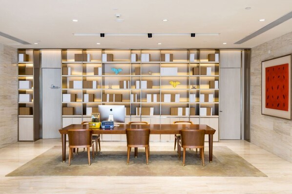 A modern library with a long table and chairs, bookshelves, and a framed picture on the wall.