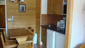 Cocina compacta con paredes de madera, una mesa de comedor, sillas, un fregadero, una cafetera y un lavavajillas.
