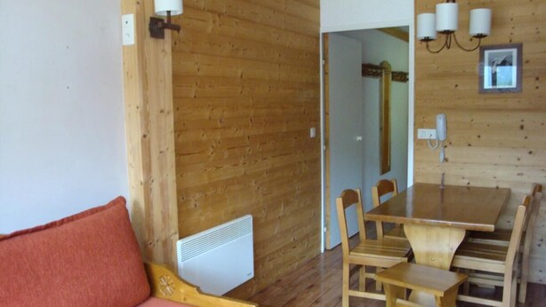 Una habitación con piso de madera, una mesa de comedor de madera con sillas, un sofá de madera y un radiador.