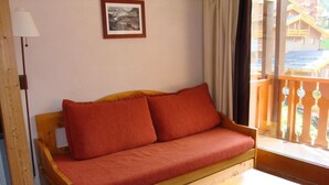 Un sofá de madera con cojines rojos, una mesita de madera y un cuadro enmarcado en la pared.