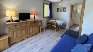 A room with a wooden dresser, a television, a table with chairs, a blue sofa, and a window with curtains. - 20m from ski slopes, 1st floor, view ski slopes, balcony, tv, 26m², Méribel-Mottaret (Méribel - Les Allues)