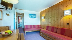 A cozy room with a wooden wall, a sofa, a table with fruit, and a TV mounted on the wall.