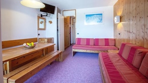 A cozy room with a wooden bench, a table with a bowl of fruit, a pink sofa, and a mounted TV.