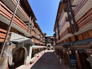 A corridor with wooden buildings, stone archways, and a clear blue sky.