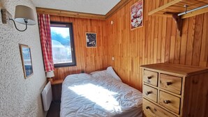 Quarto com uma cama beliche de madeira, cômoda, janela com cortina vermelha e luminária fixada na parede.