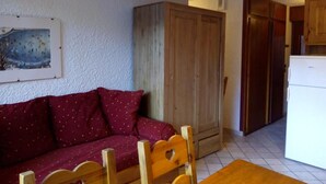 Uma sala de estar com um sofá vermelho, cadeiras de madeira, um armário de madeira e uma geladeira branca.