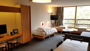 A hotel room with a bed, a desk with a computer, a TV, and a large window with a view of greenery. - 50m from ski slopes, 3rd floor, view ski slopes, balcony, tv, 65m², Les Arcs (Bourg-Saint-Maurice)