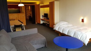 A hotel room with a bed, a sofa, a small table, a desk, and a computer. There is a door leading to a bathroom and a staircase. - 50m from ski slopes, 3rd floor, view ski slopes, balcony, tv, 65m², Les Arcs (Bourg-Saint-Maurice)