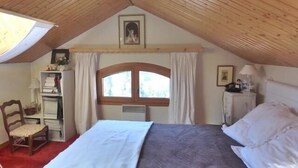 A cozy attic bedroom with a bed, a chair, a desk, and a window with curtains. - 200m from ski slopes, 4th floor, view mountain, balcony, fireplace or stove, tv, ski locker, 56m² (Méribel - Les Allues)