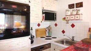 A kitchen with white cabinets, a microwave, a stove, and a sink. - 200m from ski slopes, 4th floor, view mountain, balcony, fireplace or stove, tv, ski locker, 56m² (Méribel - Les Allues)