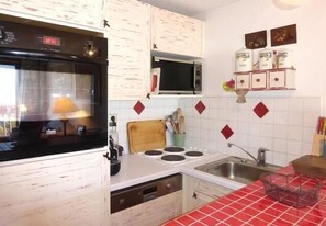 Compact kitchen with a black oven, microwave, and sink, featuring white cabinets and a distinctive backsplash.