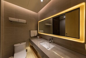 Un bany modern amb un mirall gran, un vàter, un lavabo i un para-tovallons.