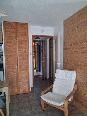 A hallway with a wooden wardrobe, a white cushioned chair, and a tiled floor.