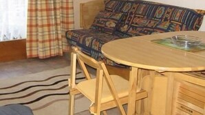 Een knus vertrek met een houten bank, een ronde houten tafel en een ruitjesgordijn.