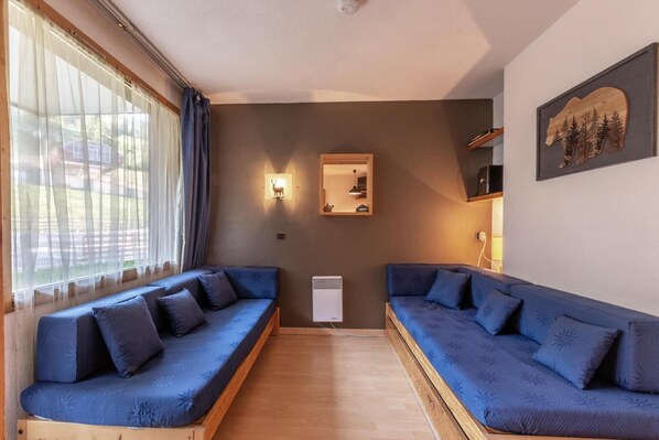 A room with two blue sofas, a small white heater, a mirror, and a wooden wall decoration.