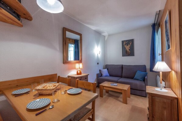Un accogliente soggiorno con un tavolo da pranzo in legno apparecchiato per due persone, un divano e un tavolino con una lampada.