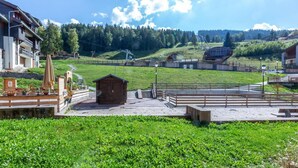 Un cadre rural avec une petite cabane en bois, un espace aménagé avec des bancs et, en arrière-plan, une colline boisée.