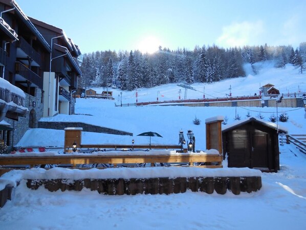 Estación de esquí nevada con edificios de madera, un puente de madera y un telesilla al fondo.