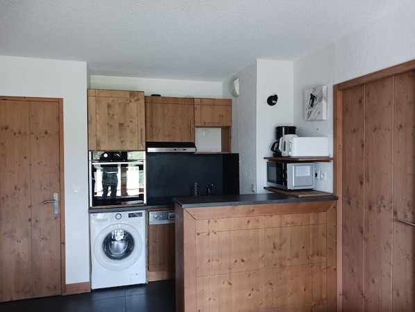 A compact kitchen with wooden cabinets, a washing machine, a microwave, and a stove.