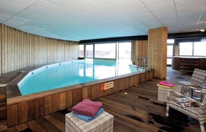 An indoor swimming pool with wooden walls and a wooden deck area with wicker chairs.