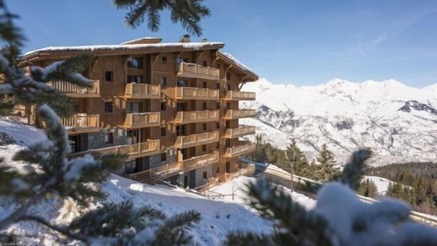 A multi-story wooden chalet with balconies, set against a backdrop of snow-covered mountains. - 2nd floor, view mountain, swimming pool, balcony, tv, ski locker, 55m², Les Arcs (Bourg-Saint-Maurice)
