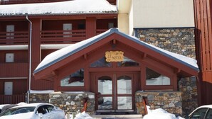 A lodge with a stone facade and a wooden entrance. There are cars parked in front, covered in snow. - 6th floor, view mountain/mountain/ski slopes, balcony, tv, ski locker, 27-26m², Les Menuires (Les Menuires)