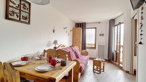 A cozy room with a wooden dining table set for two, a striped sofa, and a window with curtains. - 6th floor, view mountain/mountain/ski slopes, balcony, tv, ski locker, 27-26m², Les Menuires (Les Menuires)