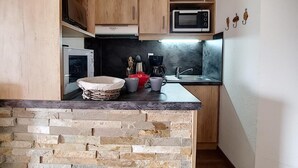 A compact kitchen with wooden cabinets, a microwave, a sink, and a stone countertop. - 6th floor, view mountain/mountain/ski slopes, balcony, tv, ski locker, 27-26m², Les Menuires (Les Menuires)