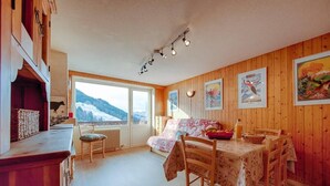 A cozy room with a wooden interior, a dining table with chairs, a bed, and a window with a mountain view. - 3rd floor, balcony, fireplace or stove, tv, 63m², Le Grand Bornand (Le Grand-Bornand)