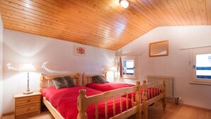 A bedroom with two wooden beds, a wooden ceiling, a nightstand, a window, and a radiator. - 3rd floor, balcony, fireplace or stove, tv, 63m², Le Grand Bornand (Le Grand-Bornand)