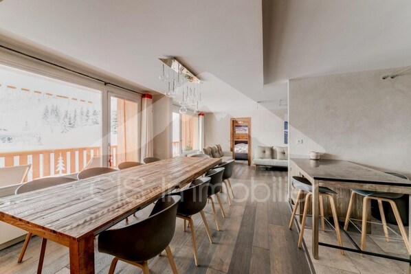 A spacious room with a long wooden table, modern chairs, and a large window with a view.