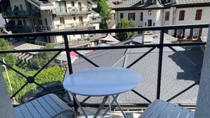 Un balcon avec une table ronde et deux chaises, donnant sur un quartier résidentiel avec des maisons et de la verdure.
