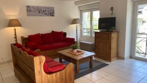 Un salon avec un canapé rouge, une table basse en bois et un téléviseur posé sur un meuble en bois.