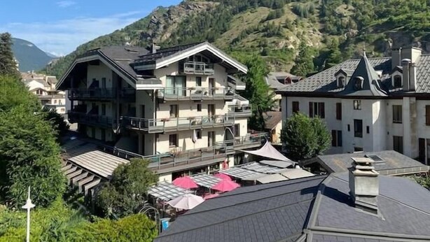 Un immeuble à plusieurs étages doté de balcons, entouré de verdure et de montagnes.