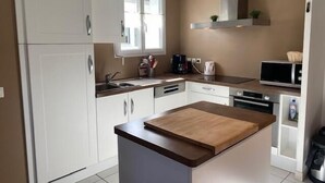 Une cuisine moderne avec des meubles blancs, un îlot central doté d’un plan de travail en bois, un four à micro-ondes et une bouilloire posés sur le plan de travail.