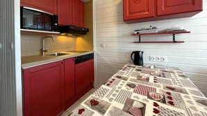 Une cuisine de taille réduite avec des placards rouges, un four à micro-ondes, un évier et un sol à motifs.