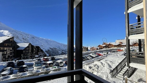 Une vue depuis un balcon donnant sur un parking, avec un sol enneigé et des bâtiments en arrière-plan.