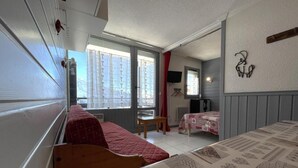 Une petite pièce comprenant un lit, une petite table et une fenêtre avec des rideaux.
