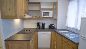 A compact kitchen with wooden cabinets, a microwave, a coffee maker, and a dishwasher.