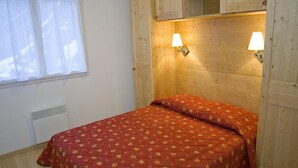 Un dormitorio con cabecera de madera, dos lámparas fijadas a la pared, una ventana con cortinas blancas y una cama con colcha estampada.