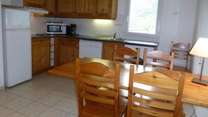 Cocina compacta con armarios de madera, microondas, lavavajillas y una mesa de comedor con sillas.