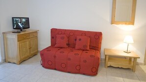 Una habitación pequeña con un sofá rojo, un armario de madera, un televisor y una mesita de noche con lámpara.